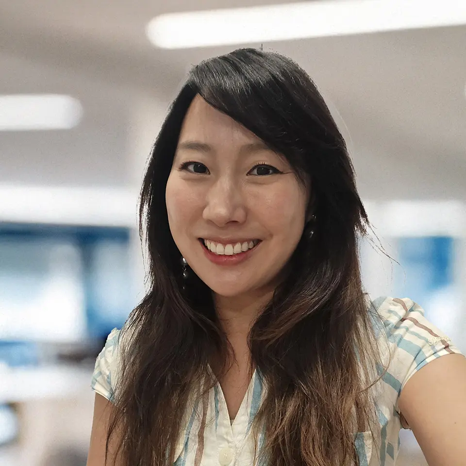 Smiling woman with long hair in an office setting, wearing a striped shirt.