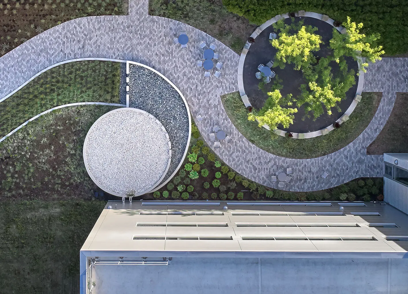 Aerial view of a modern landscaped garden with circular and curved paths, seating areas, and greenery.