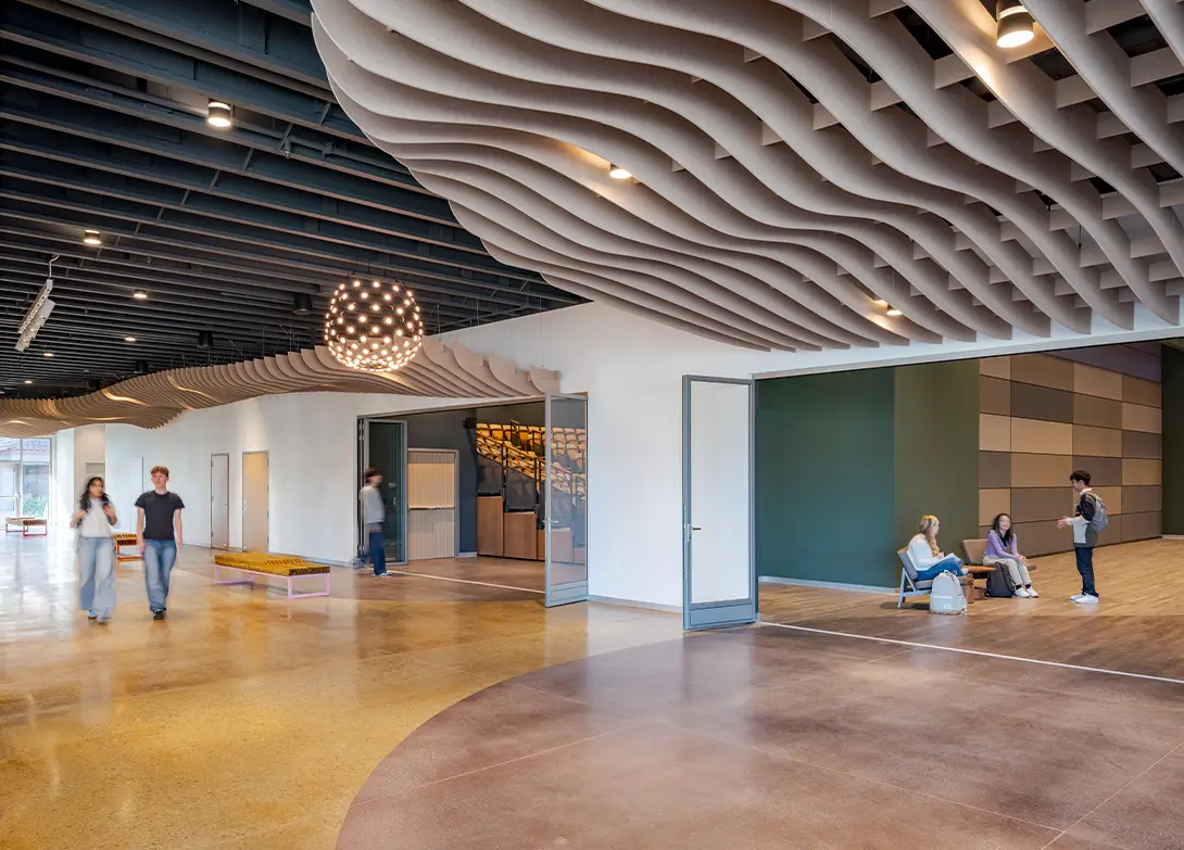 Modern lobby with wave ceiling, hanging lights, and people conversing, highlighting open design and social interaction.