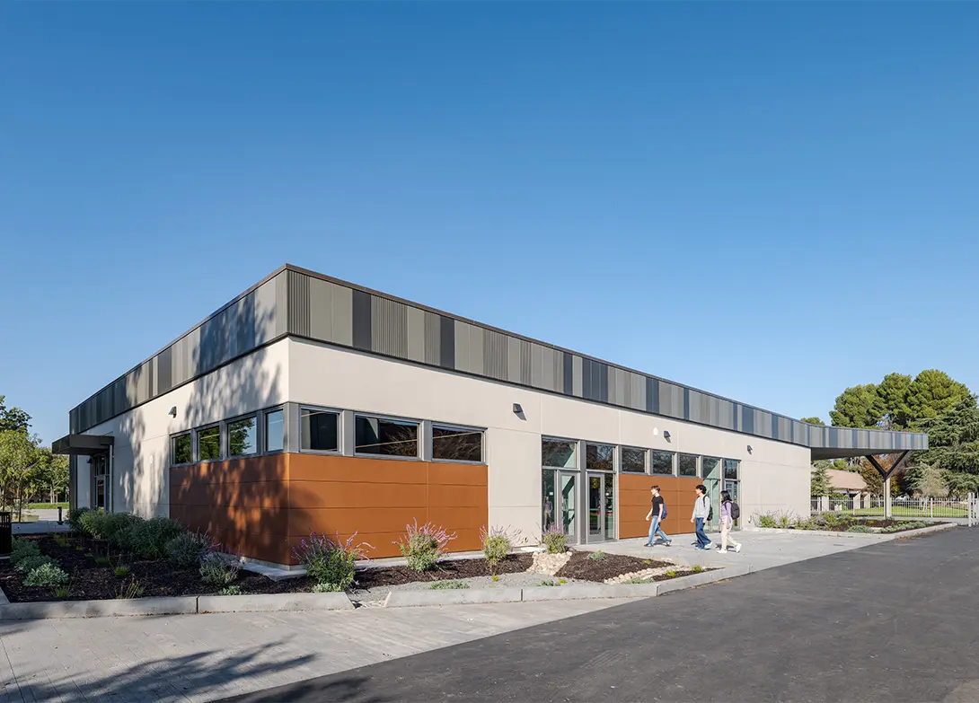 Modern educational building with clear blue sky, students walking outside, and green landscaping elements.
