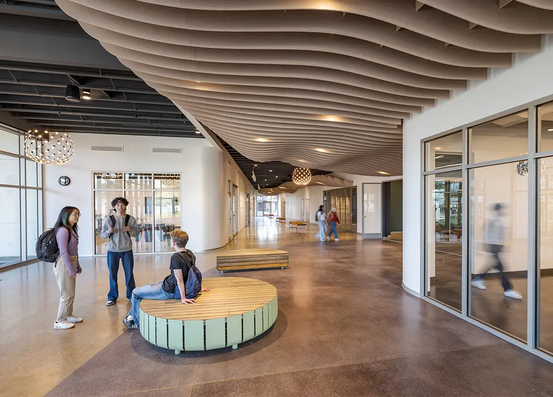 Modern school hallway with students, open seating, large windows, and wavy ceiling design.