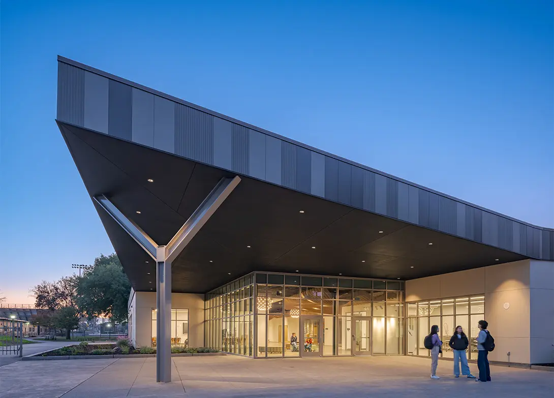 Modern building entrance at dusk with people standing outside under large overhang.