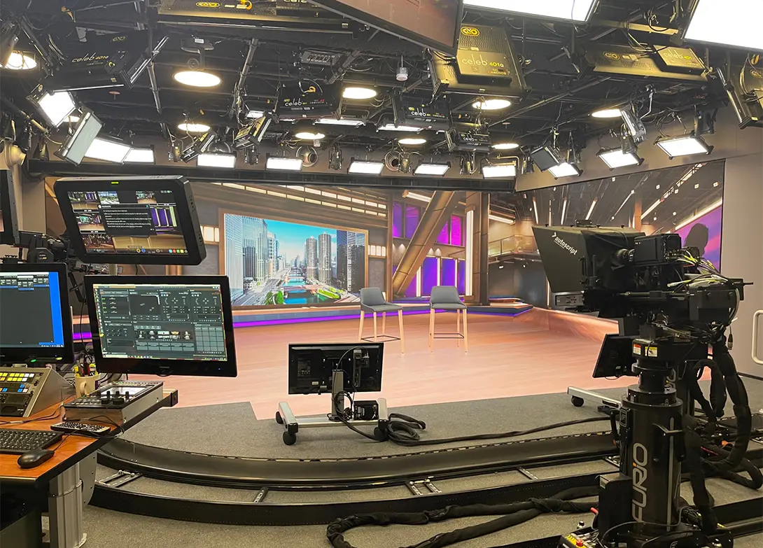Modern TV studio setup with cameras, lights, monitors, and a cityscape background on a large screen.