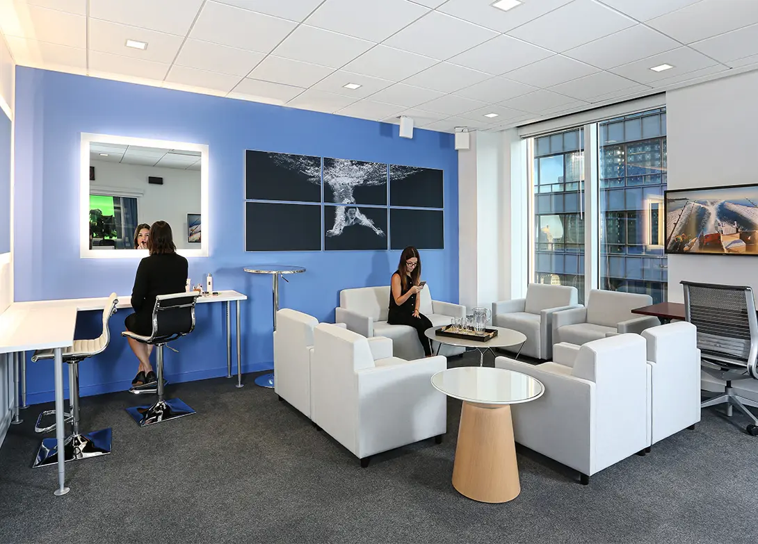 Modern office lounge with blue accent wall, comfy seating, and large windows, creating a relaxed, productive atmosphere.