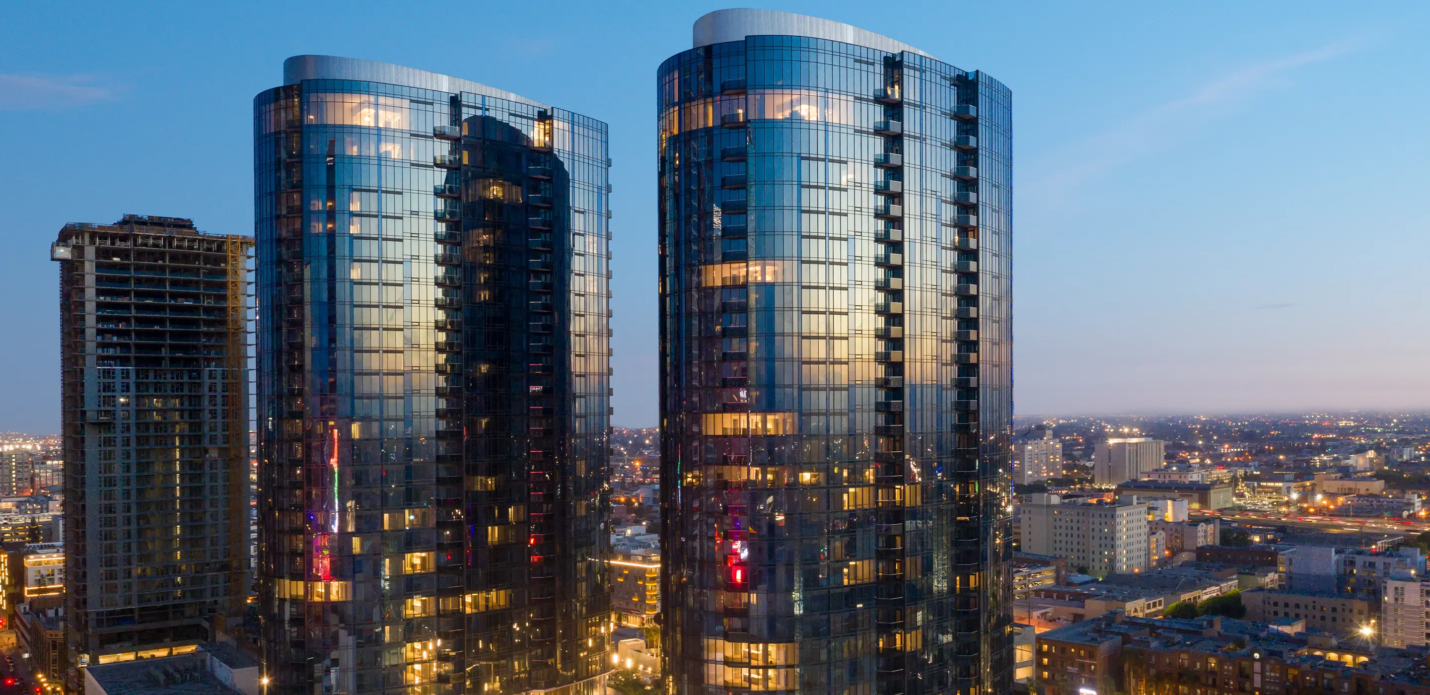 Modern skyscrapers at twilight with city lights, reflecting the sunset on glass facades in an urban skyline.