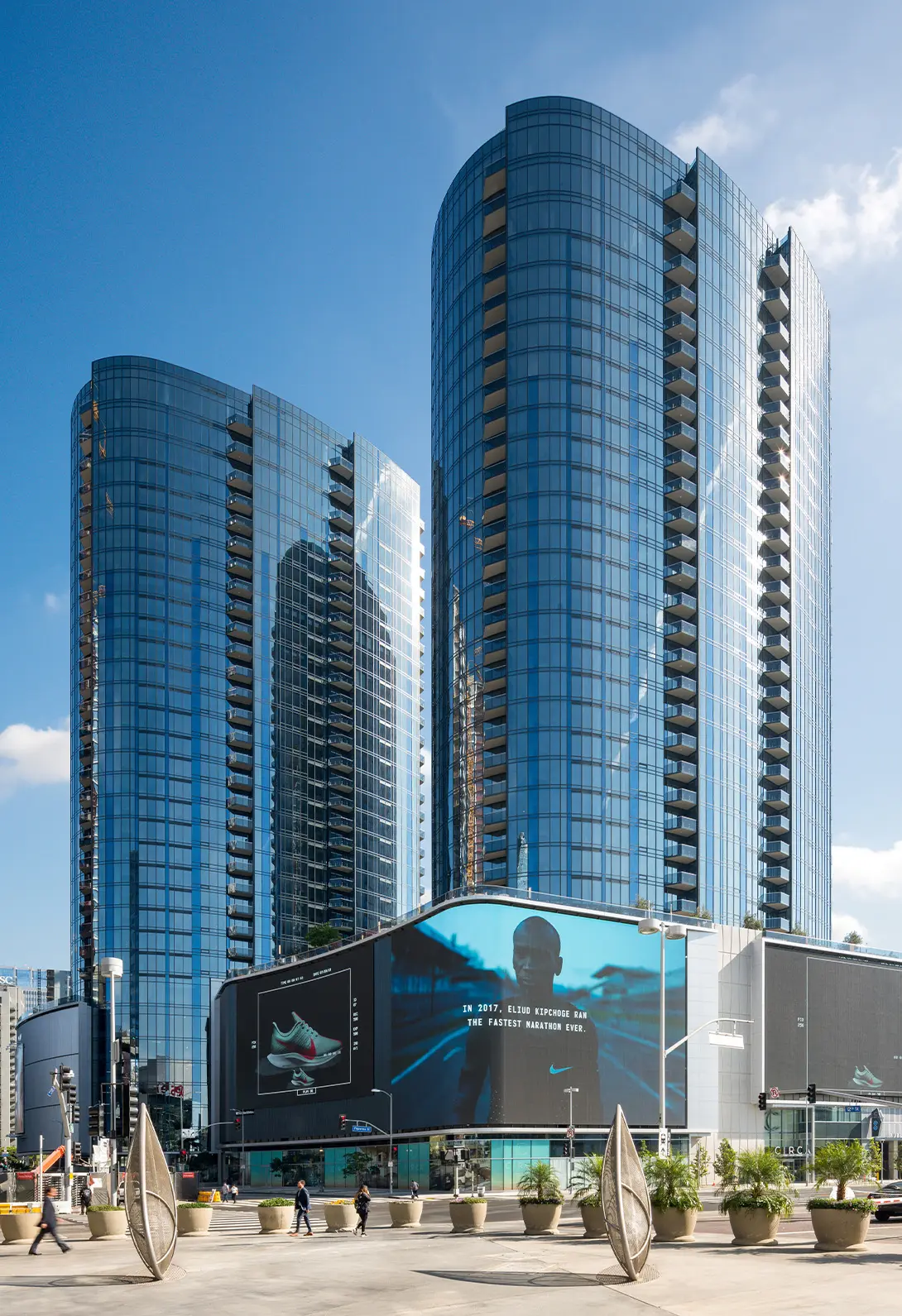 Modern skyscrapers with glass facades and a large digital billboard in an urban setting.
