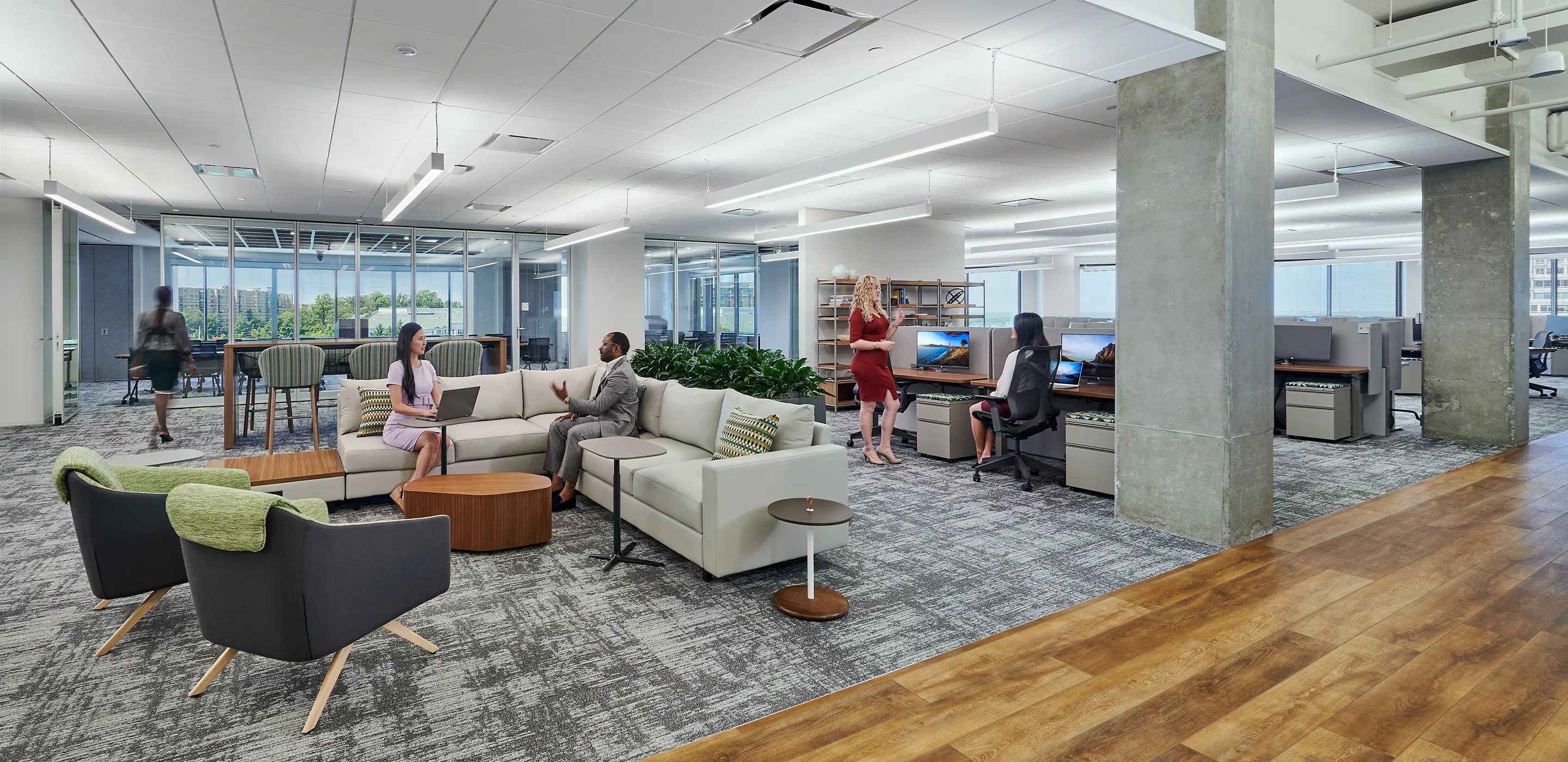 Modern open office space with collaborative seating, green plants, and professionals engaged in work and conversation.