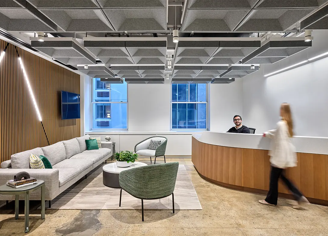 Modern office lobby with sofa, chairs, reception desk, and geometric ceiling design. Welcoming and stylish interior.