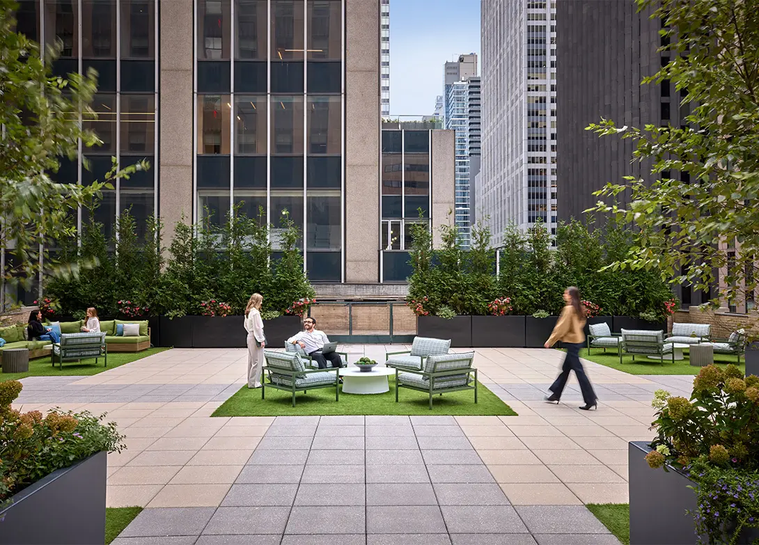 Rooftop terrace with people relaxing on outdoor furniture, surrounded by plants and city skyscrapers.