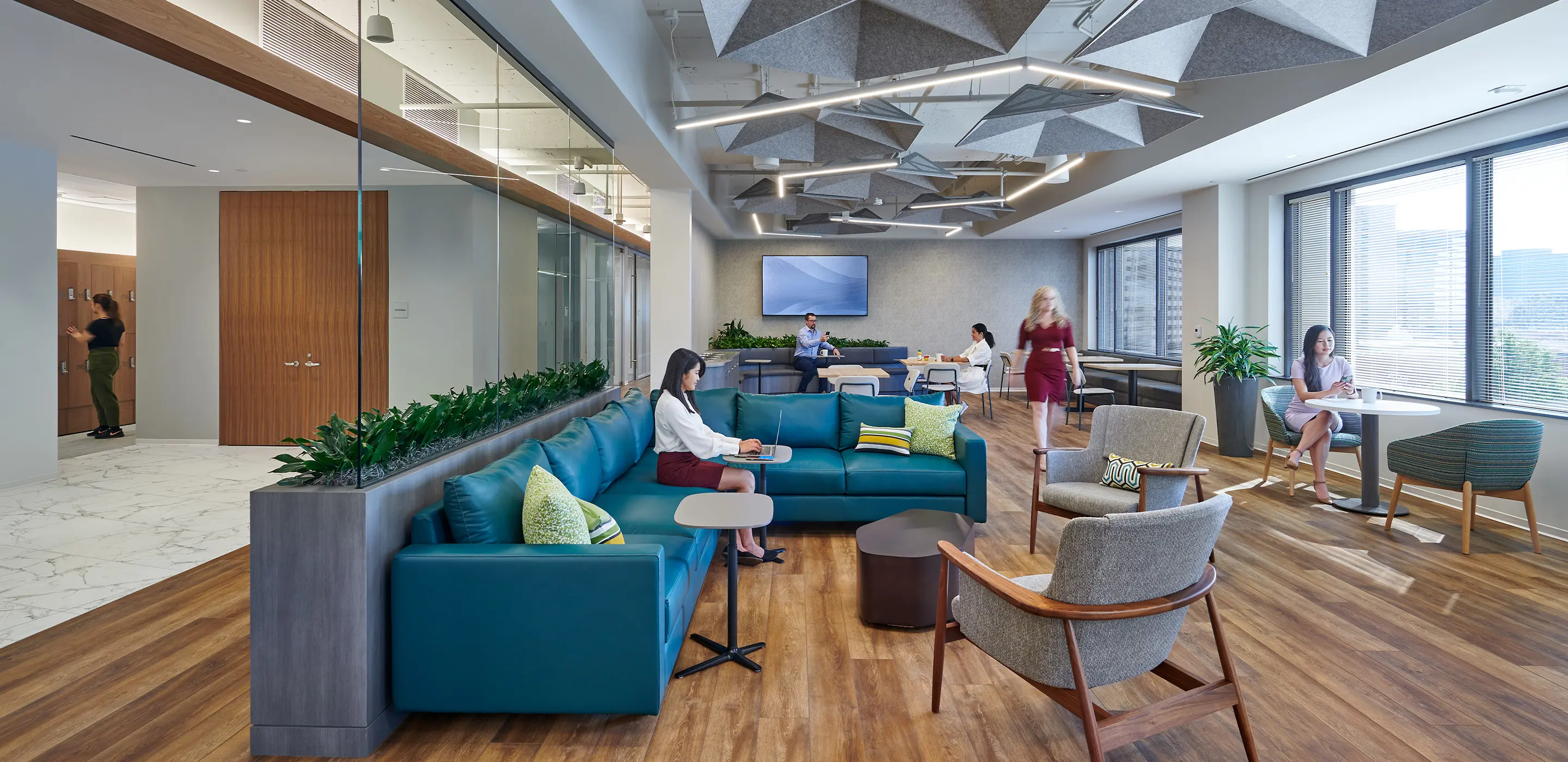 Modern office lounge with people working and relaxing on couches and tables, featuring stylish decor and natural light.
