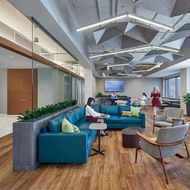 Modern office lounge with blue sofas, geometric ceiling panels, and people working and conversing, featuring a cozy atmosphere.
