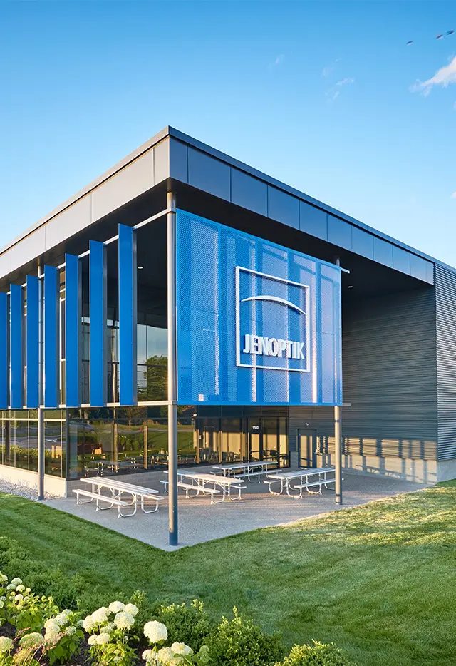 Modern corporate building with blue facade, featuring the Jenoptik logo, surrounded by greenery under a clear sky.
