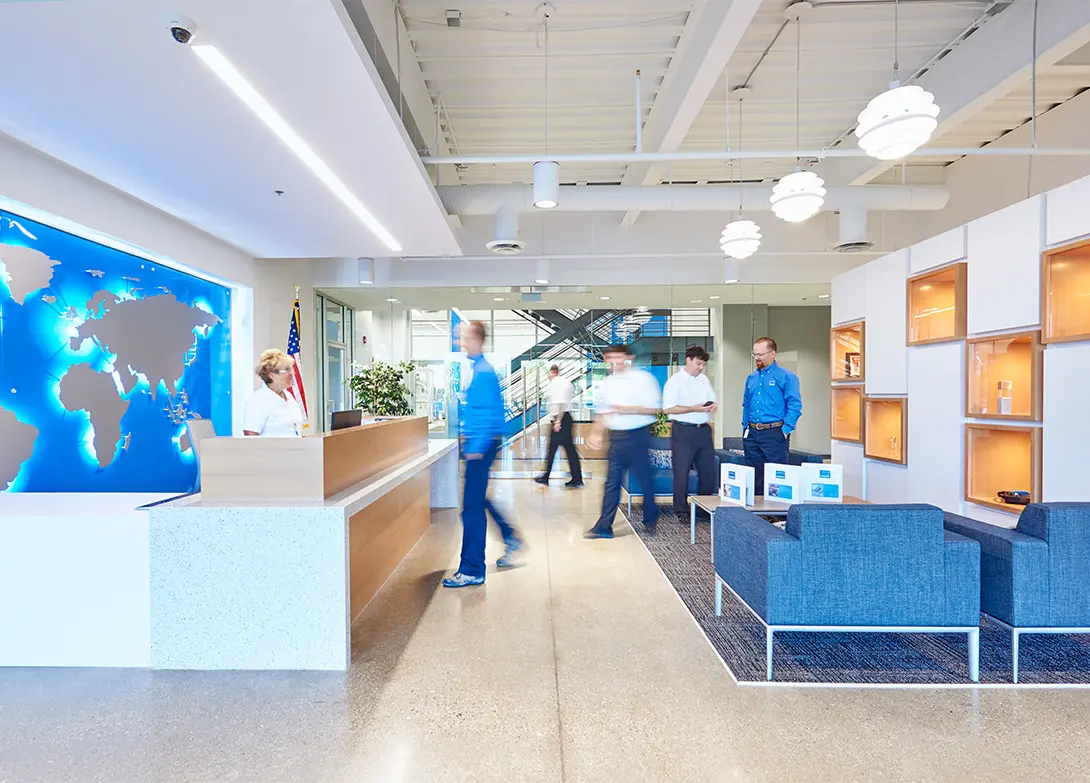 Modern office lobby with people interacting, featuring a receptionist, world map, and seating area.