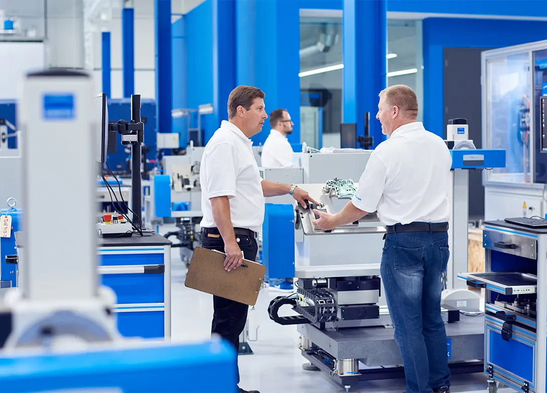 Technicians discussing machinery in a high-tech manufacturing facility with blue accents.