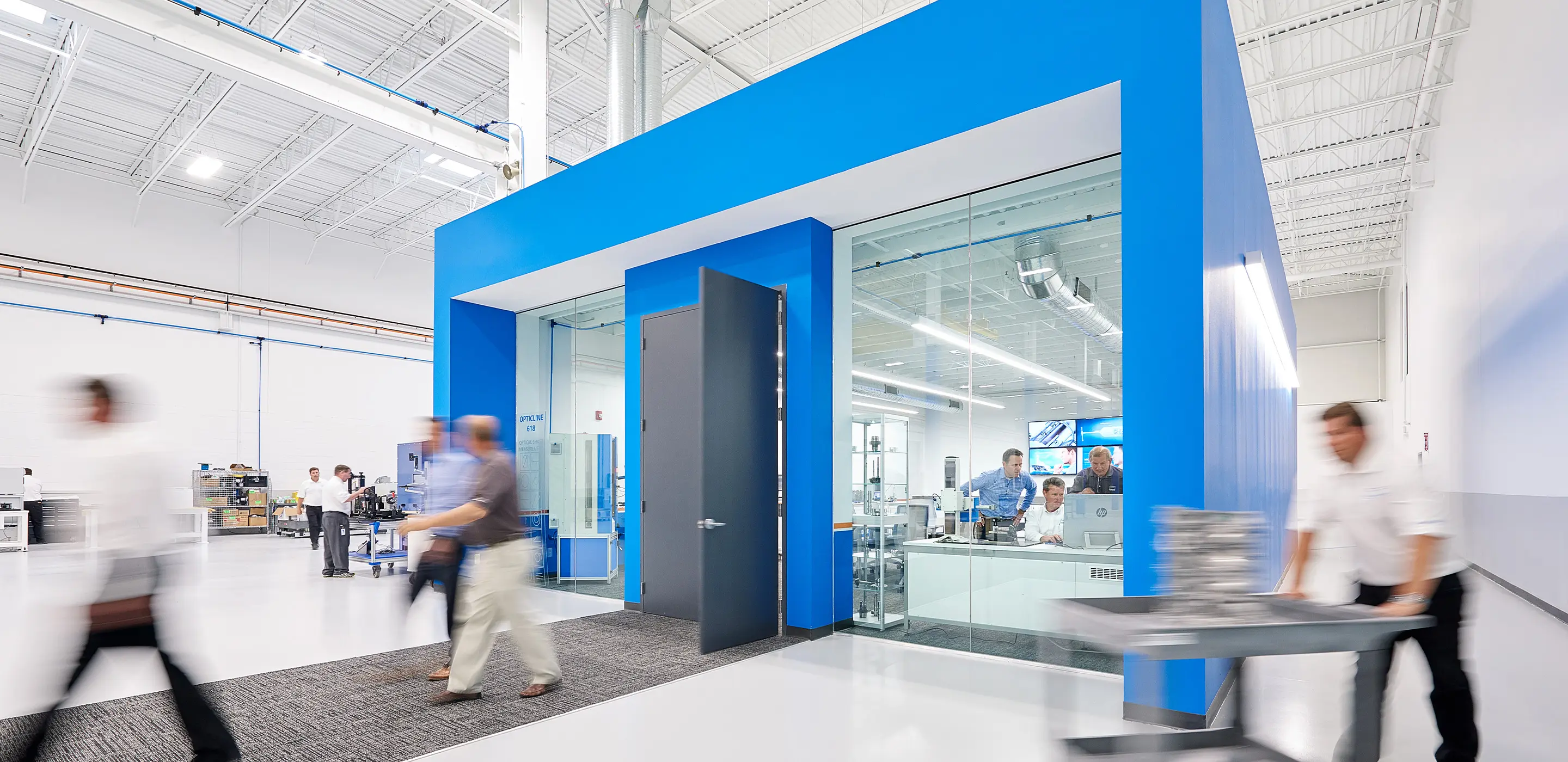 Modern office with glass walls, workers in motion, blue accents, and industrial decor.