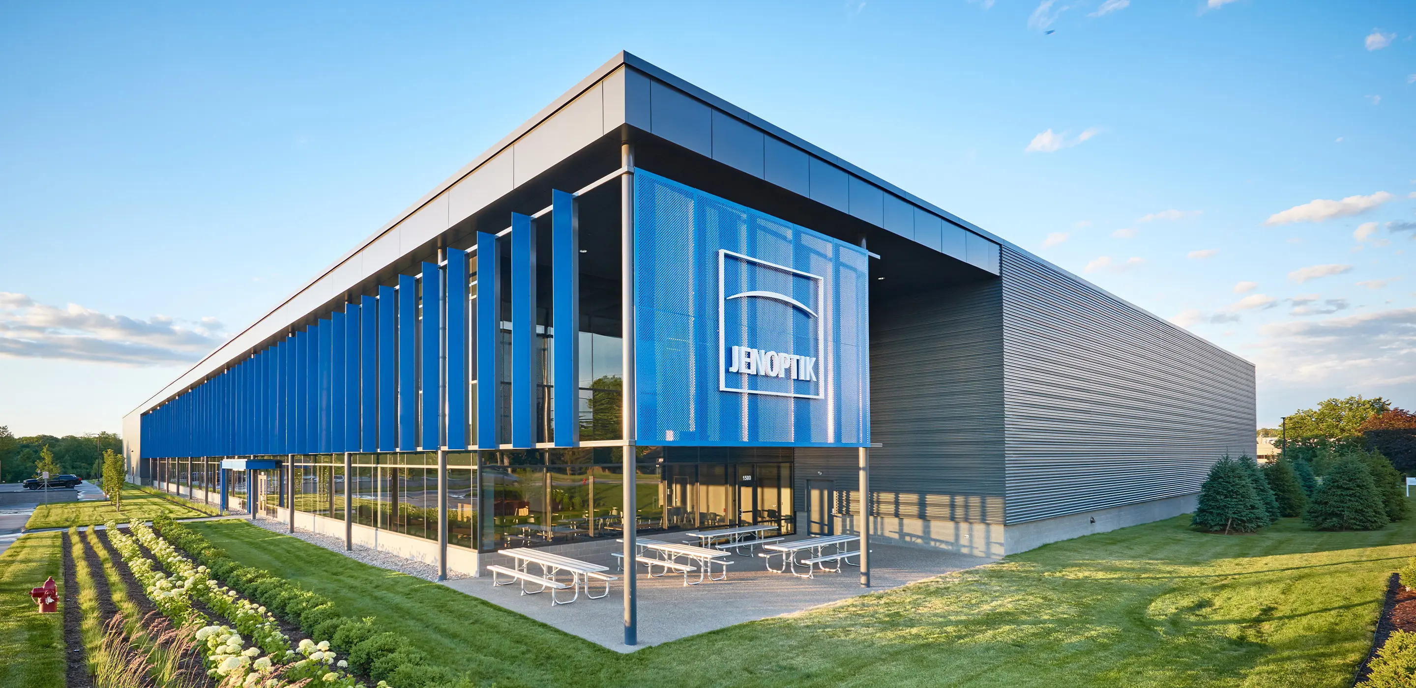 Modern office building with blue glass facade, surrounded by green landscape, under a clear blue sky.