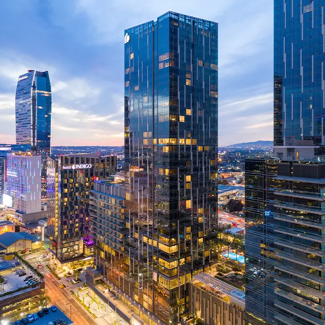 Aerial view of modern skyscrapers and cityscape at sunset, with illuminated windows reflecting a vibrant urban atmosphere.