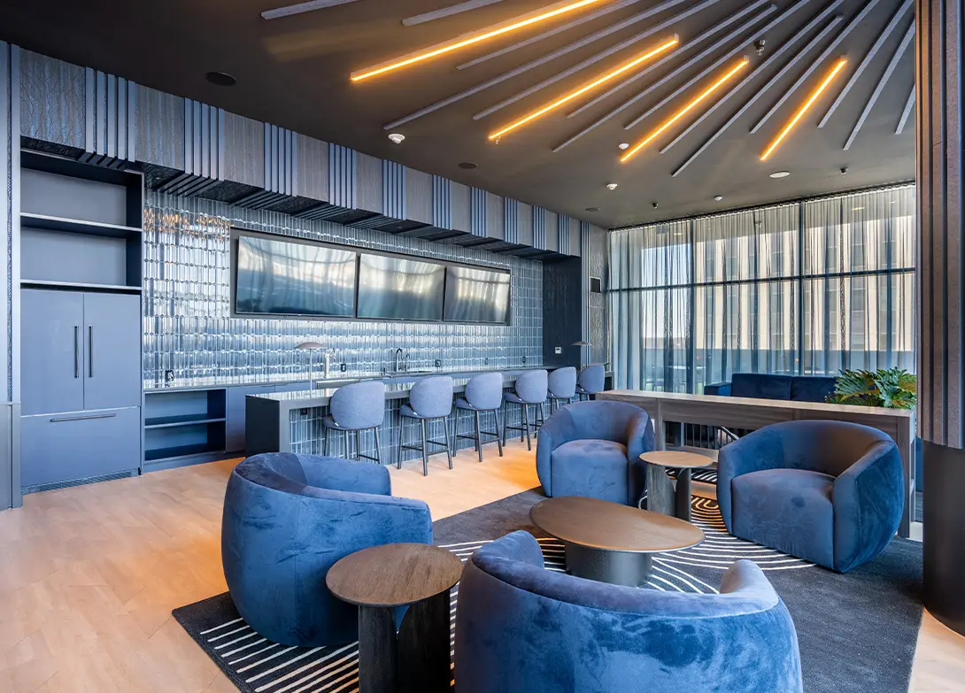 Stylish modern lounge with blue chairs, wooden tables, and sleek bar area under artistic lighting and ceiling design.