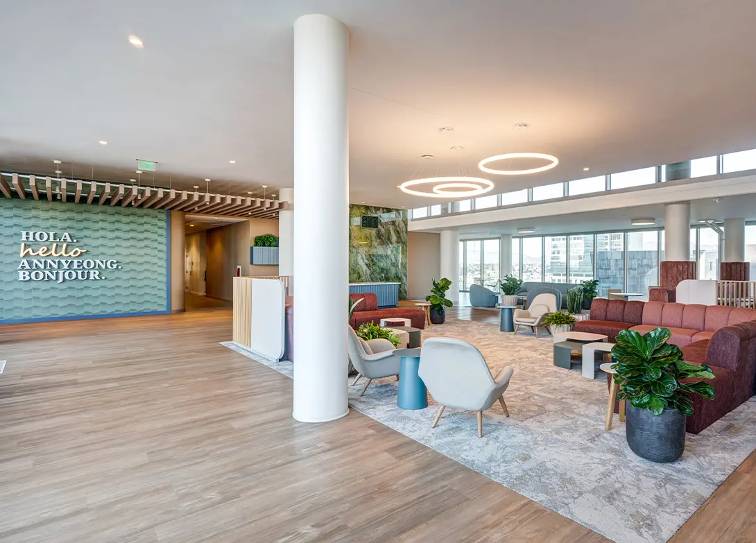 Modern office lobby with stylish seating, circular lighting, greenery, and a multilingual welcome wall greeting visitors.