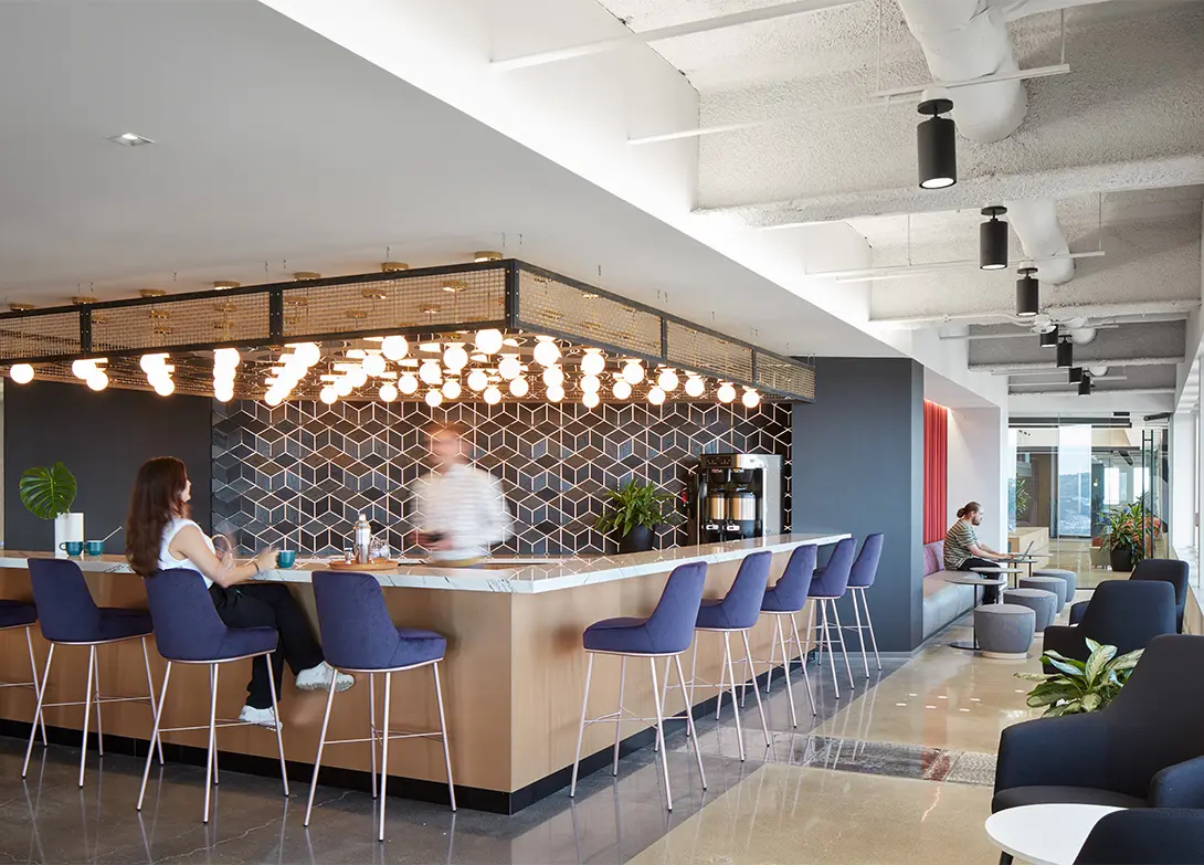 Modern office lounge with contemporary hexagonal tile design, stylish bar seating, and people enjoying a relaxed atmosphere.