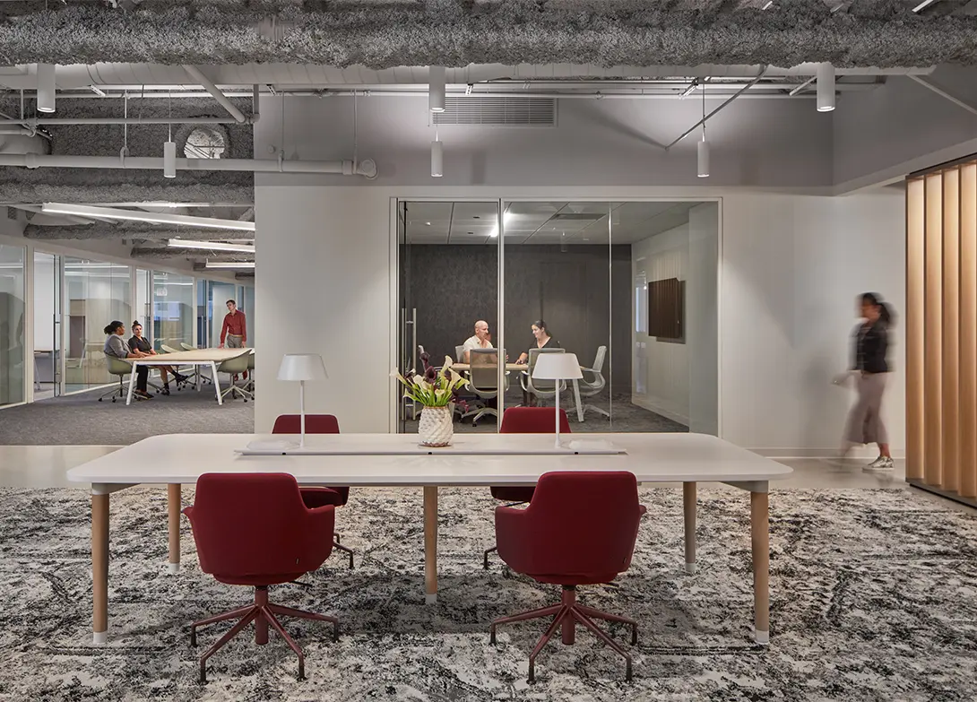 Modern office space with red chairs, conference rooms, and people working collaboratively.