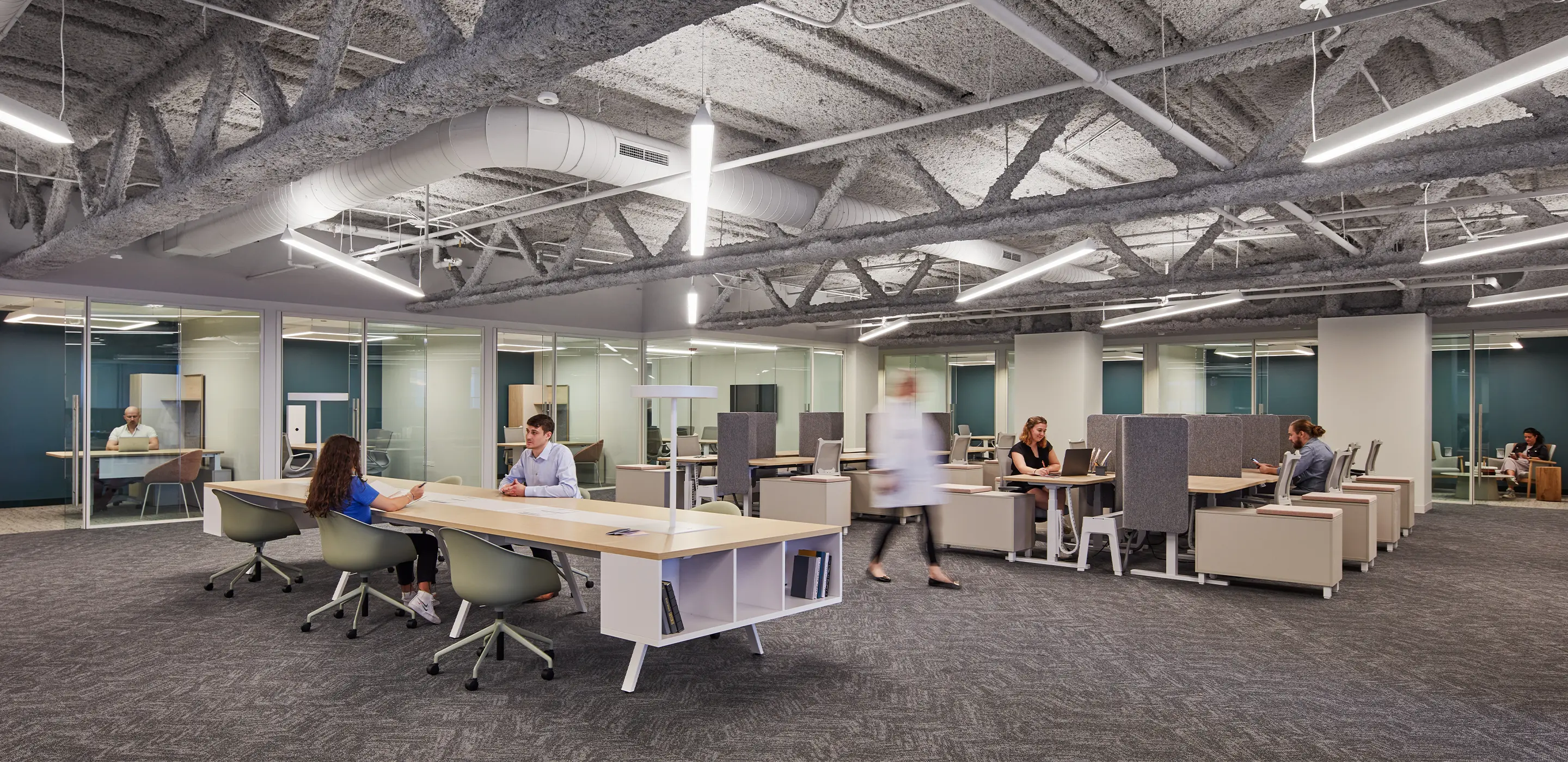 Modern open office space with employees working at shared desks and private cubicles.