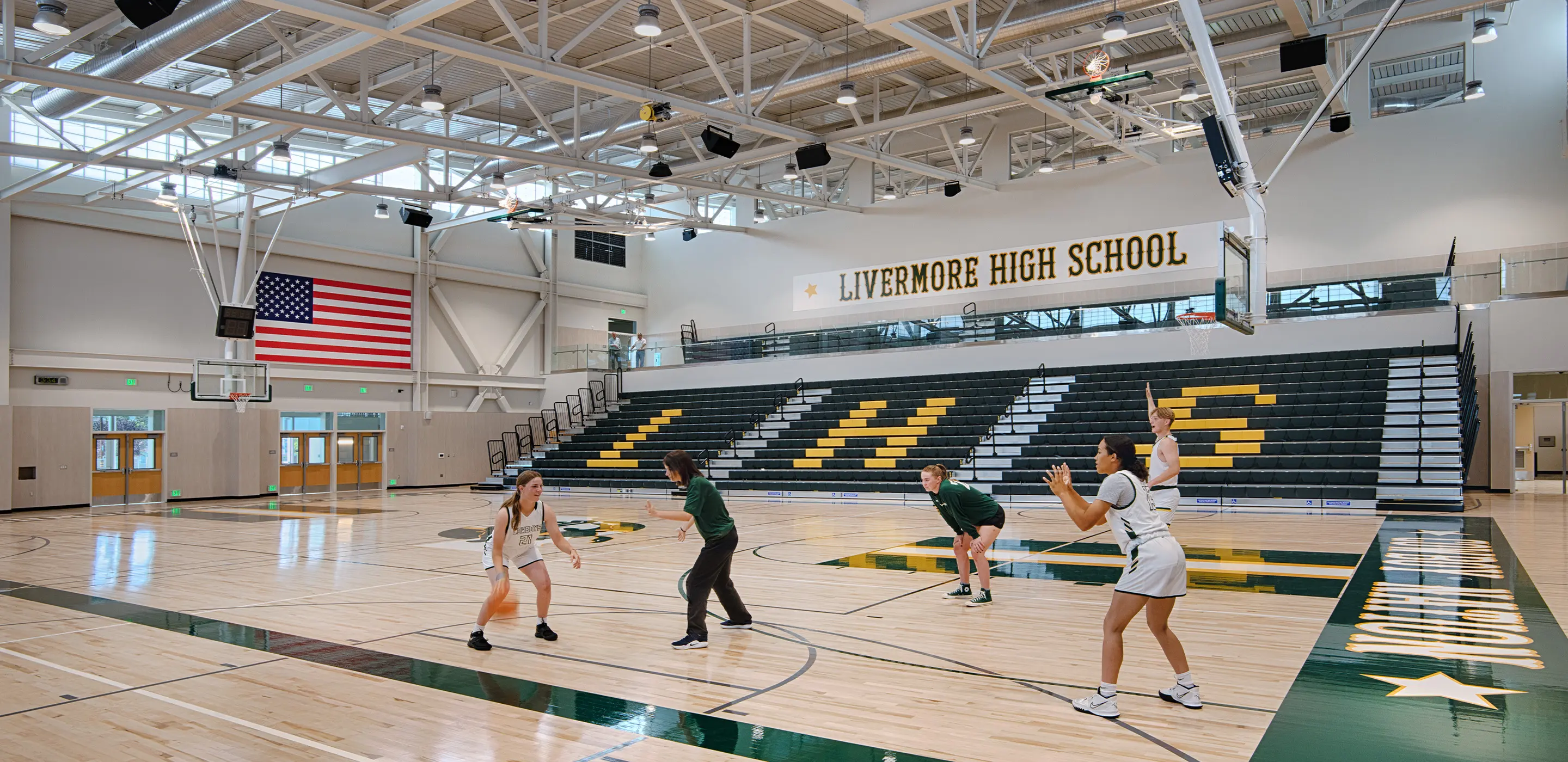 High school basketball practice in a gym with players and coaches, Livermore High School banner in background.