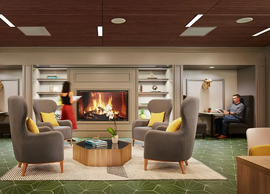 Cozy lounge with fireplace, modern chairs, and a person reading, creating a warm and inviting atmosphere.