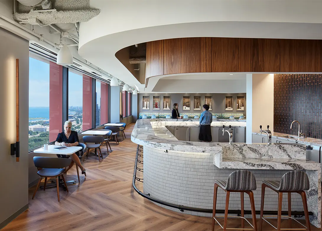 Modern office kitchen with a sweeping city view, featuring elegant furniture and a cozy seating area.