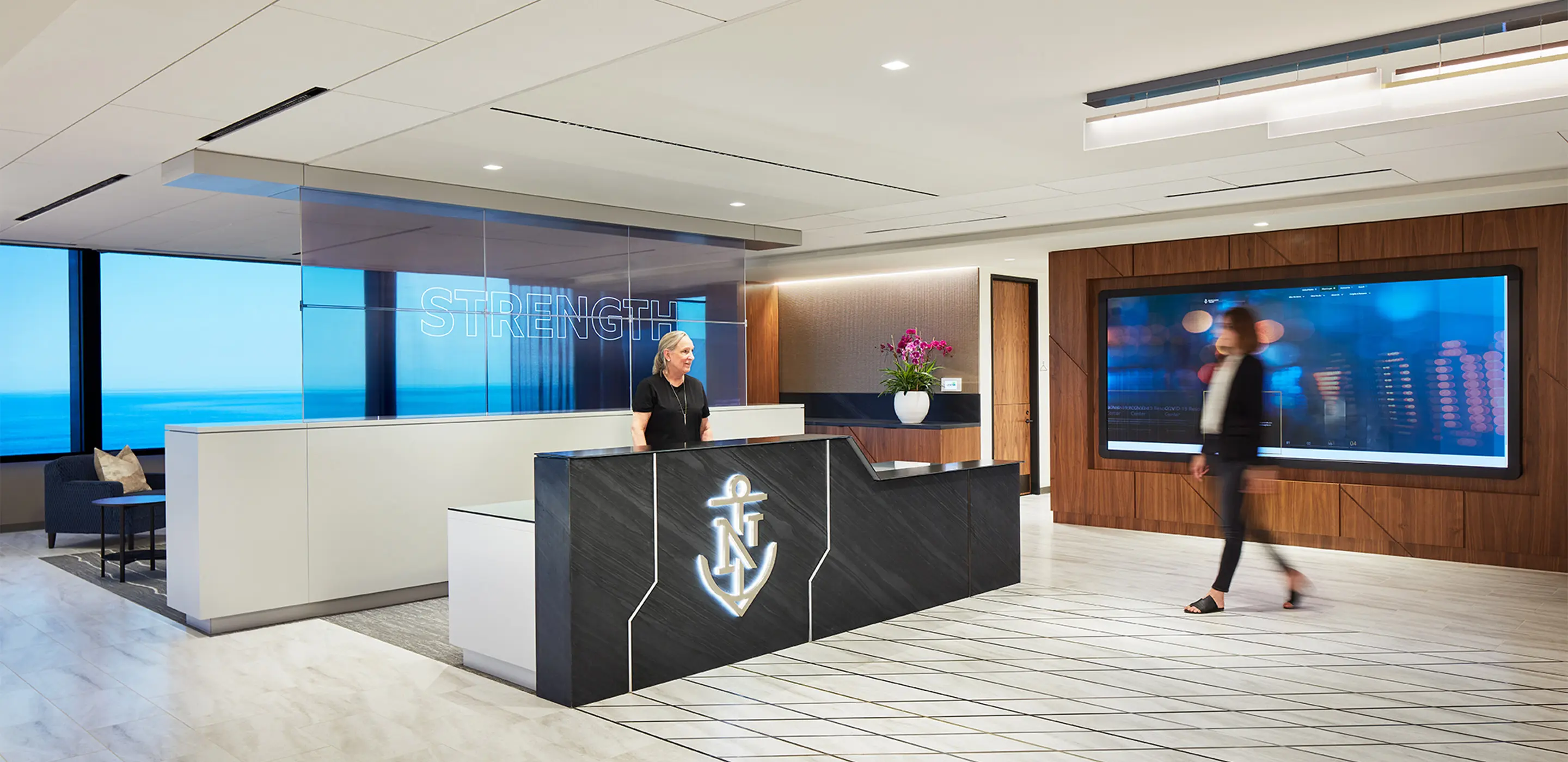 Modern office reception with ocean view, sleek design, and digital display.