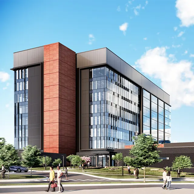 Modern office building with glass facade and red accents, surrounded by trees and people walking on a sunny day.