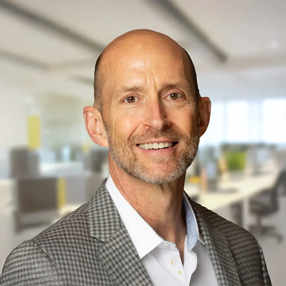 Smiling man in a suit with a blurred office background.