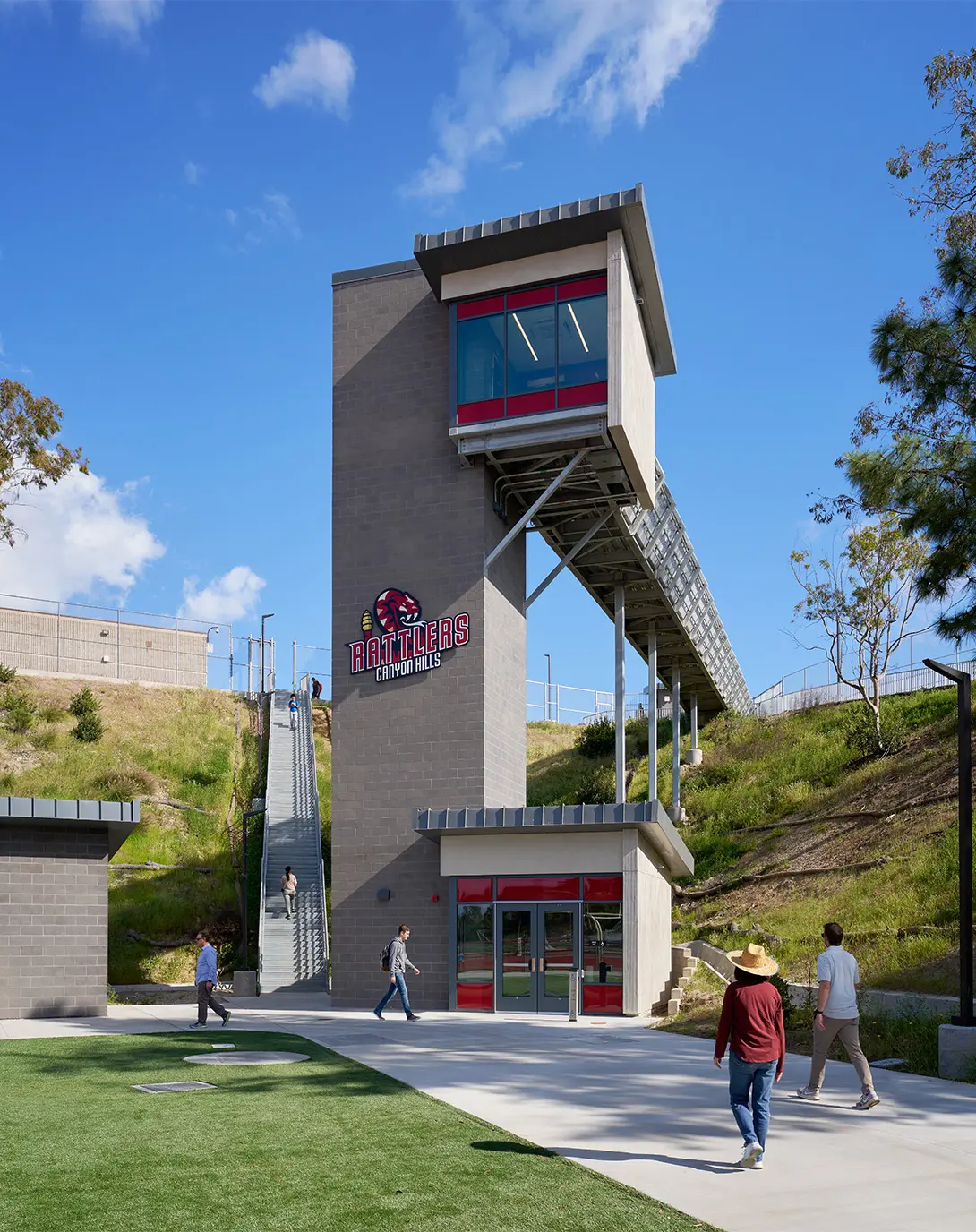 Modern school building with Rattlers Canyon Hills logo, surrounded by greenery, under a clear blue sky.