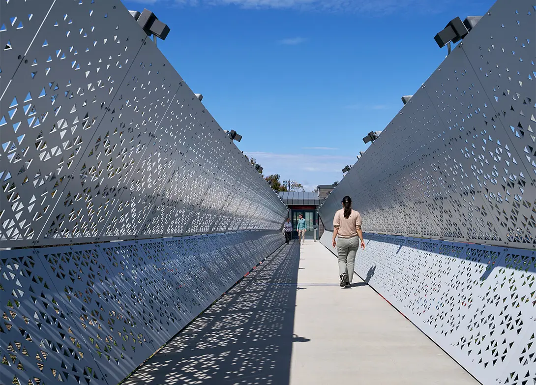 Person walking along a modern, architectural walkway with geometric patterns under a clear blue sky.