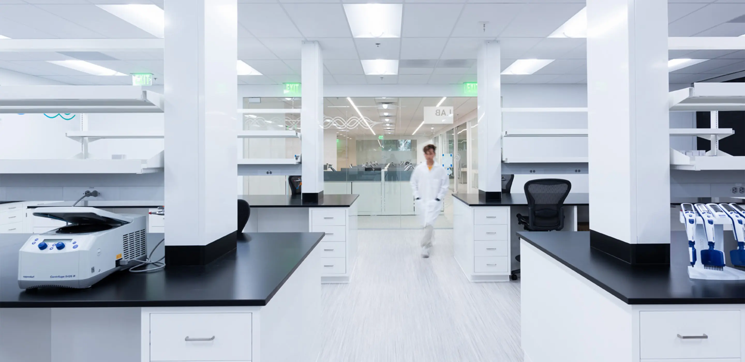 Modern laboratory with scientific equipment and a technician in a white coat walking through the space.