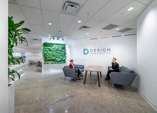 Modern office lobby of Design Therapeutics with two people seated, green wall, and stylish furnishings.