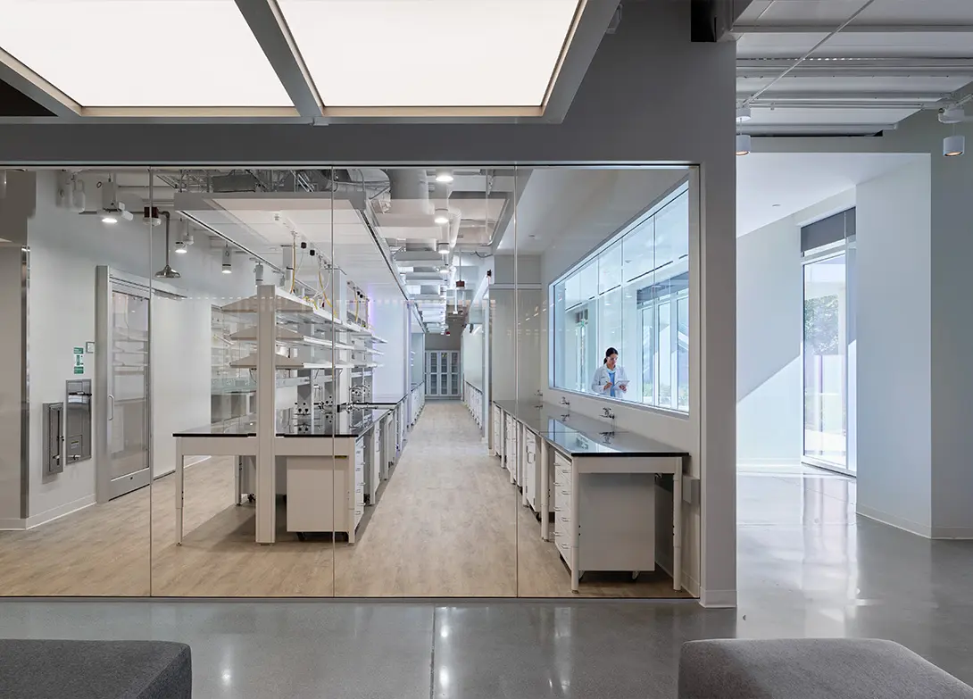 Modern laboratory interior with glass walls, well-organized workstations, and a scientist in a white coat.