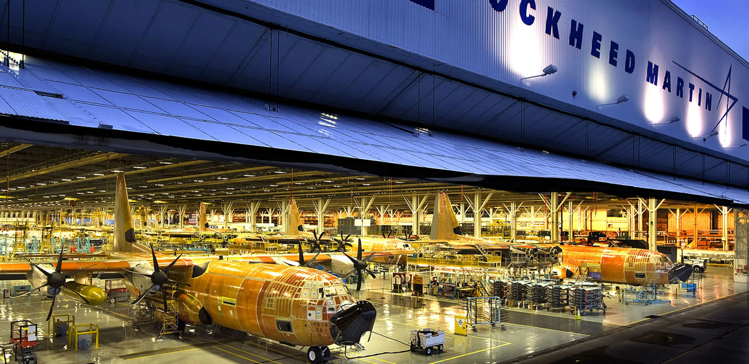 Aircraft assembly inside Lockheed Martin factory hangar at night.