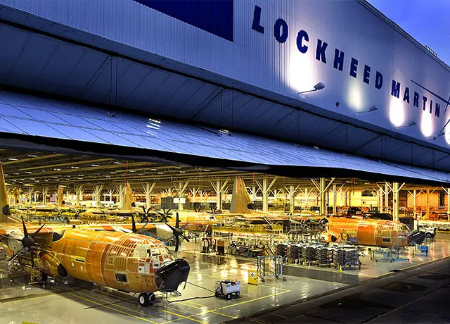 Lockheed Martin aircraft production hangar illuminated at night, displaying multiple aircraft in assembly stages.