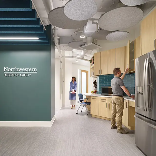 Modern research safety office with teal walls and kitchen area, featuring a man reaching into a cabinet.