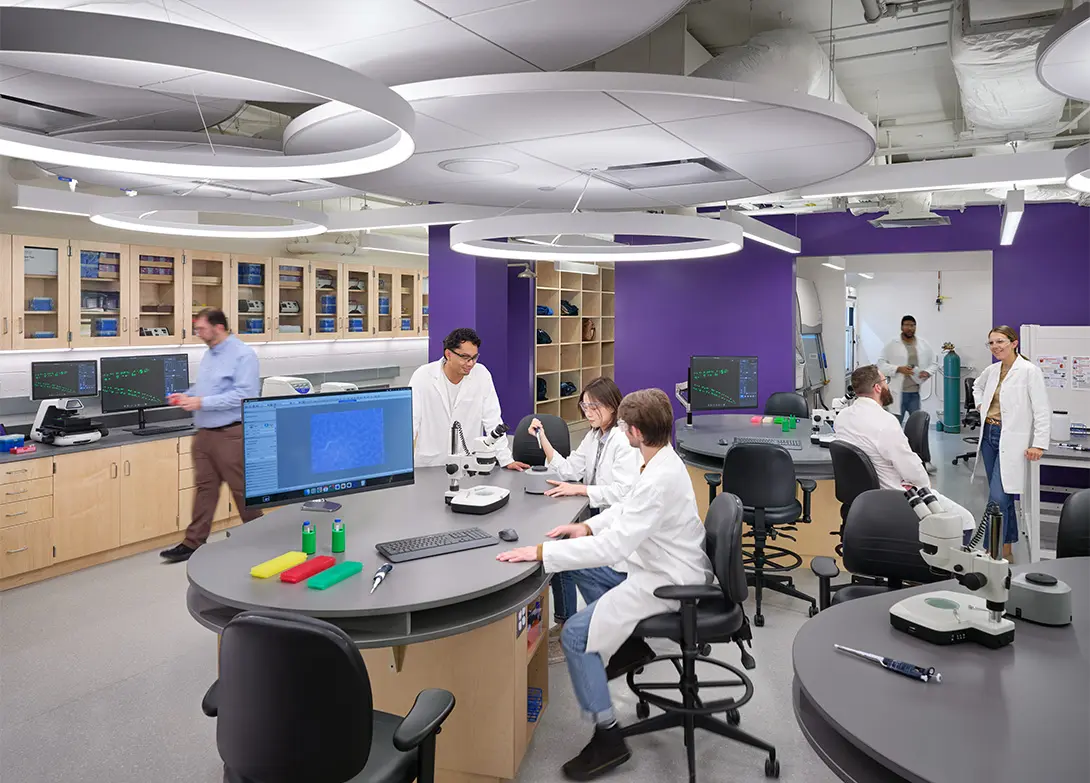 Scientists collaborating in a modern laboratory with computers and microscopes, engaging in research and discussion.