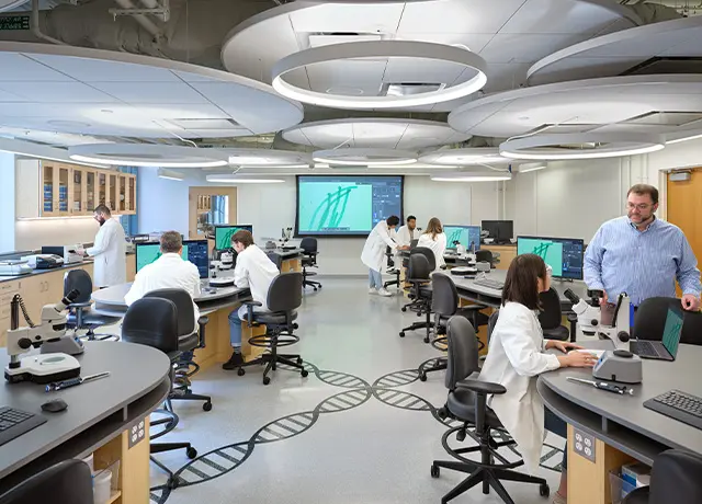Modern lab with scientists in white coats conducting research at workstations with computers and microscopes.