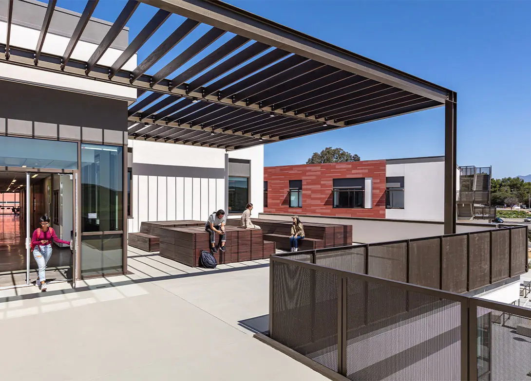 Modern school courtyard with students, featuring outdoor seating, an open sky view, and contemporary architectural design.