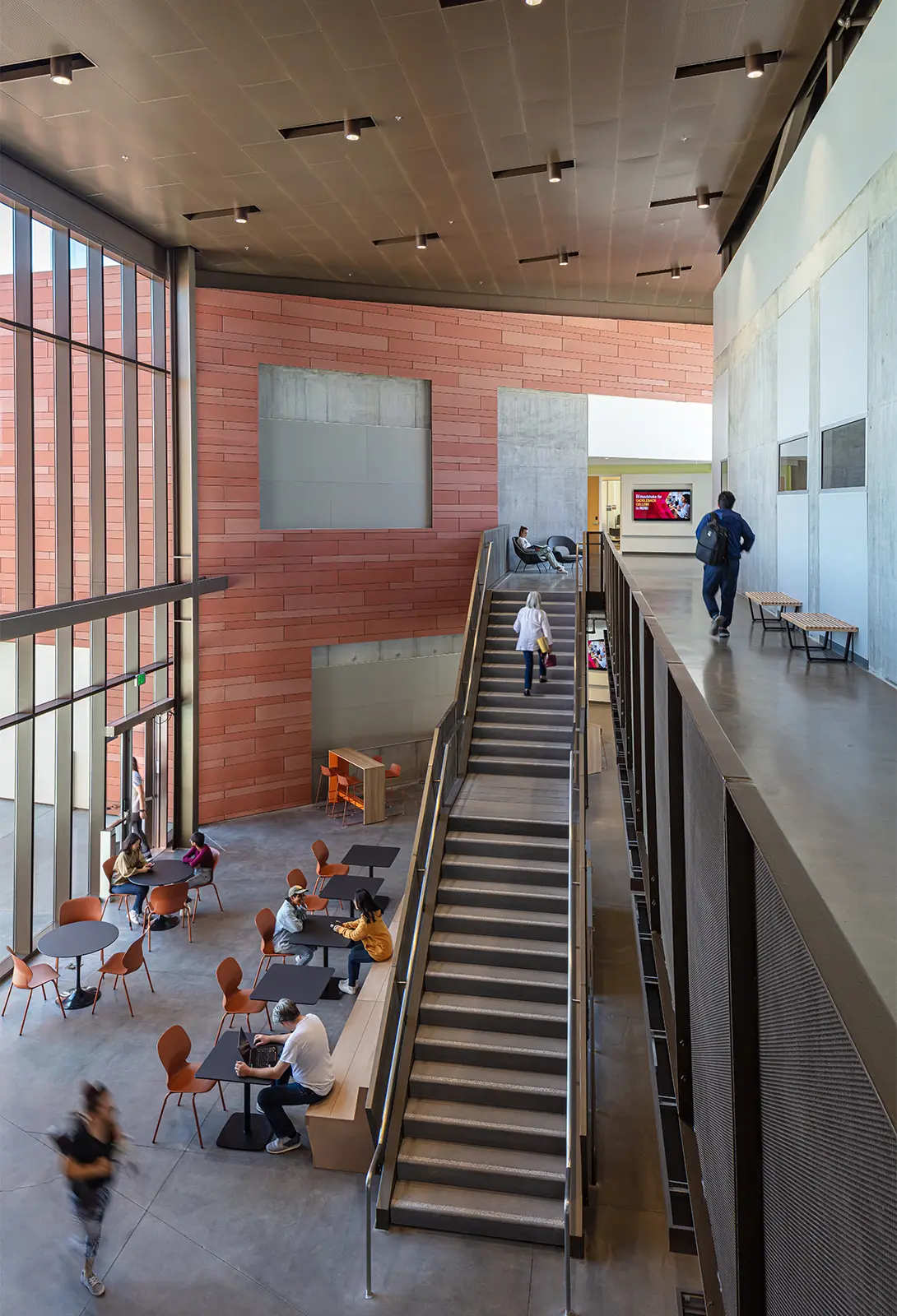 Modern interior with stairs, large windows, and people studying in a spacious common area at a university building.