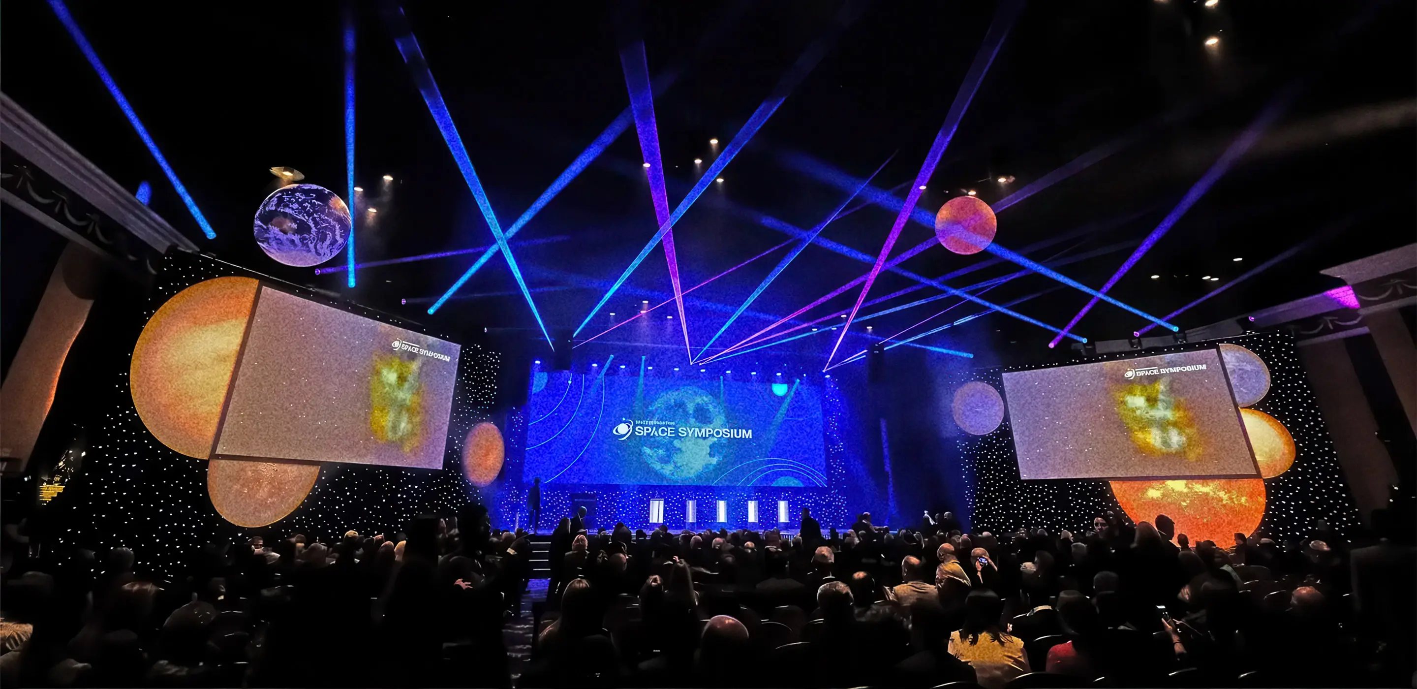 Space Symposium event with colorful lights, space-themed decor, and large audience in a conference hall.