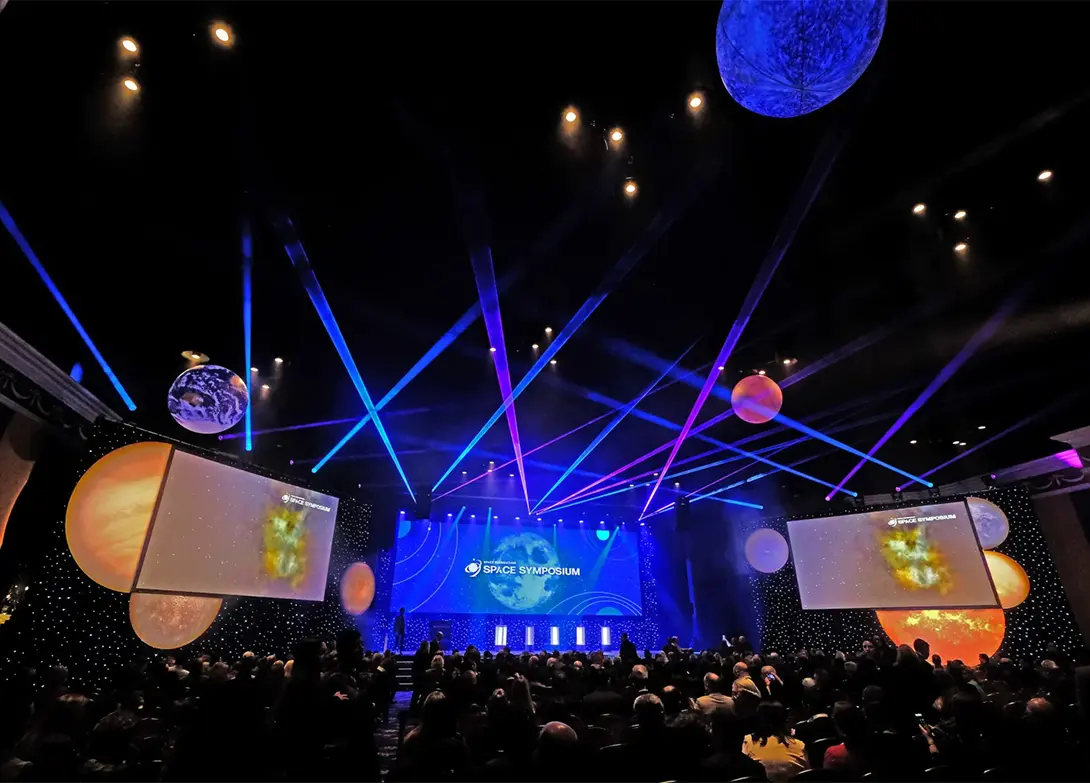 Space symposium event with colorful lights, planet displays, and a crowd in a dimly lit auditorium.