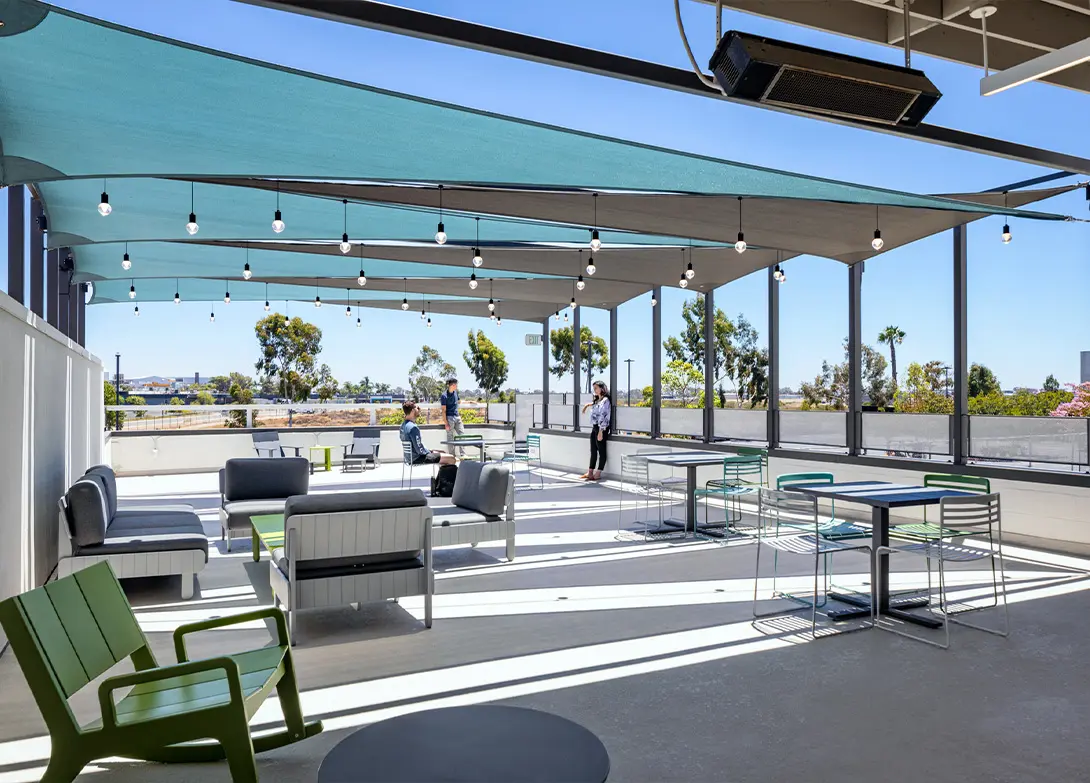 Outdoor rooftop lounge with seating, shade sails, and string lights, offering a modern space for relaxation and socializing.