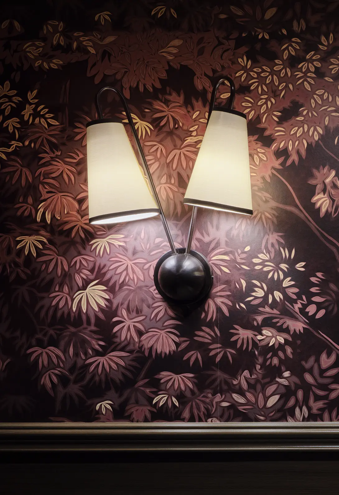 Elegant wall sconce with dual lamps against a floral-patterned wallpaper, creating a cozy ambiance.