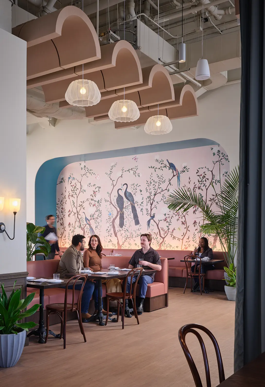 Chic café interior with modern decor, featuring a bird-themed mural and people enjoying a cozy dining experience.