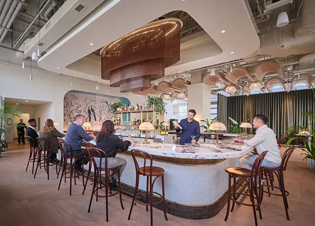 Modern cafe with people enjoying drinks at a stylish bar counter, decorated with hanging lights and plants.